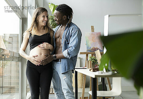 Glücklicher Mann berührt Bauch einer lächelnden schwangeren Frau zu Hause