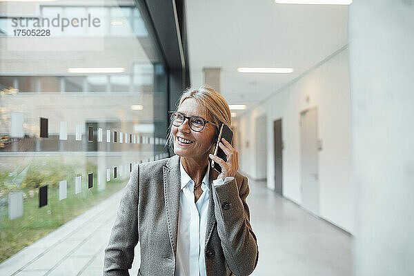 Lächelnde Geschäftsfrau  die im Büro auf dem Smartphone spricht