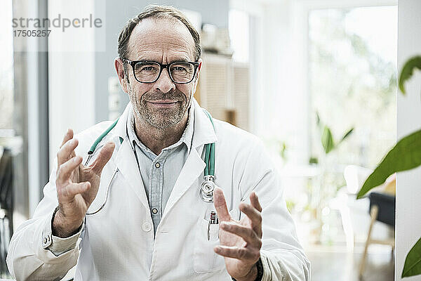 Lächelnder Arzt mit Brille gestikuliert in der Klinik