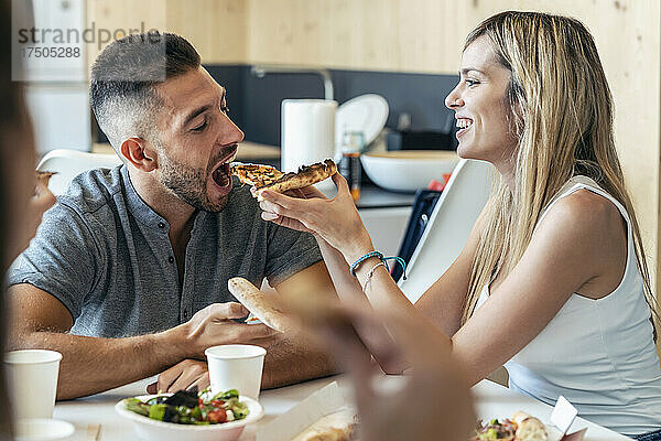 Blonde Geschäftsfrau füttert Geschäftsmann im Büro mit Pizza