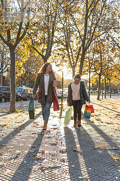 Mutter und Tochter gehen im Herbst mit Einkaufstüten auf dem Fußweg spazieren