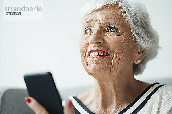 Lächelnde ältere Frau mit Smartphone zu Hause