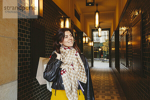 Lächelnde Frau hält Einkaufstüten am Flur