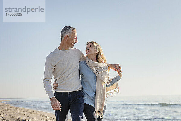 Frau mit Schal schaut Ehemann am Strand an