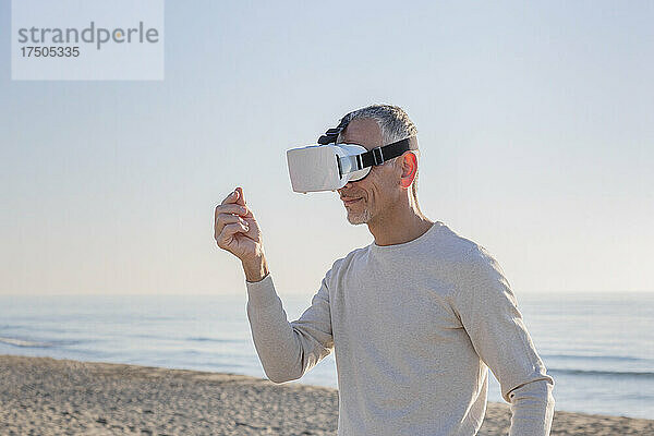 Mann mit Virtual-Reality-Headset gestikuliert am Strand