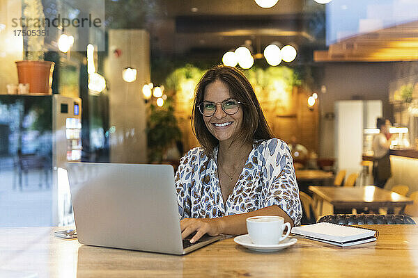 Lächelnder Freiberufler mit Laptop im Café sitzend
