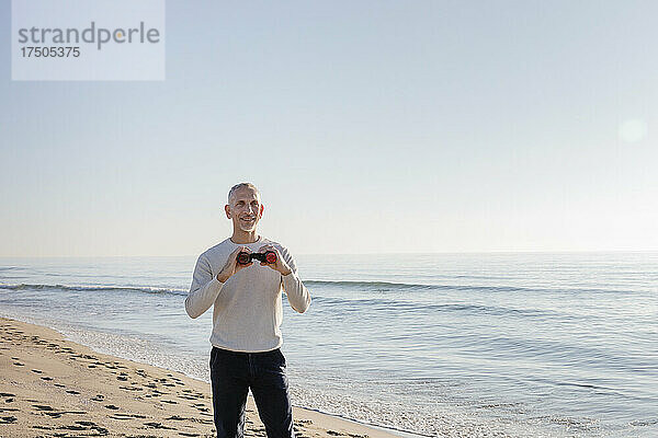 Mann mit Fernglas steht am Strand