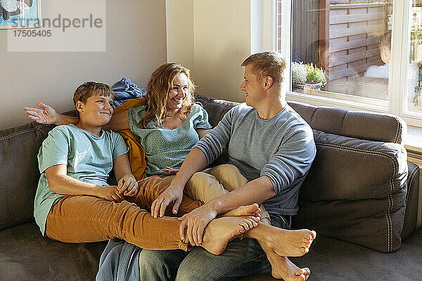 Lächelnde Frau spricht zu Hause mit Mann und Sohn auf dem Sofa