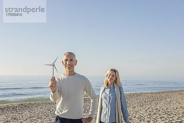 Mann hält Windturbinenmodell und steht mit seiner Frau am Strand