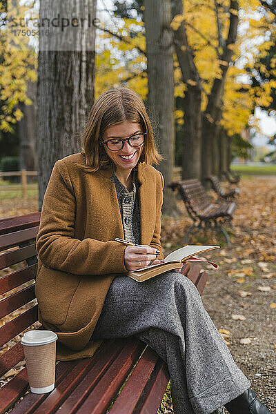 Lächelnde Frau schreibt im Herbstpark in ein Buch