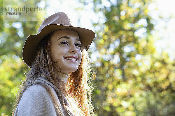 Lächelnde  nachdenkliche Frau mit Hut im Wald
