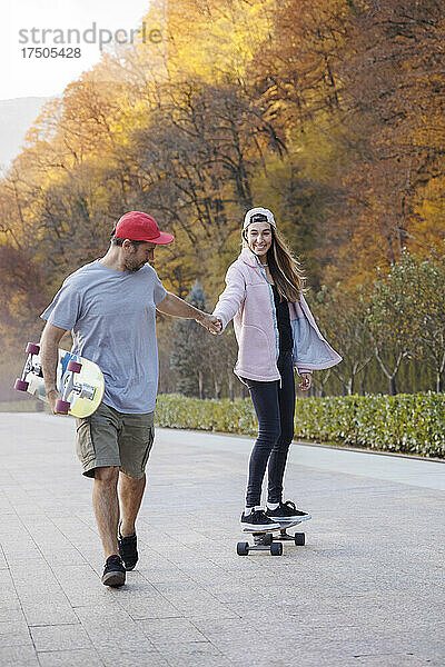 Mann geht und hält die Hand einer Frau beim Skateboarden auf dem Fußweg
