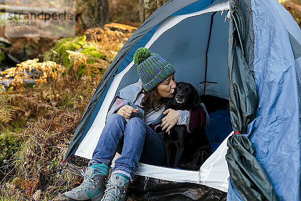 Frau küsst Labrador Retriever im Zelt im Wald