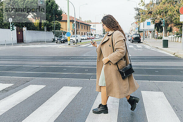 Plus-Size-Frau benutzt Smartphone beim Überqueren der Straße