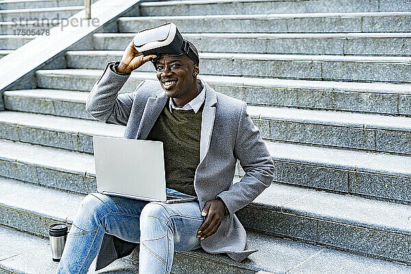 Geschäftsmann mit Virtual-Reality-Headset sitzt mit Laptop auf Stufen