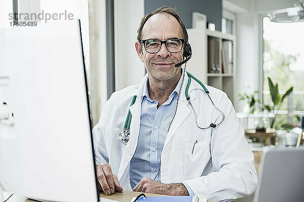 Lächelnder Arzt vor Computermonitor in der Klinik