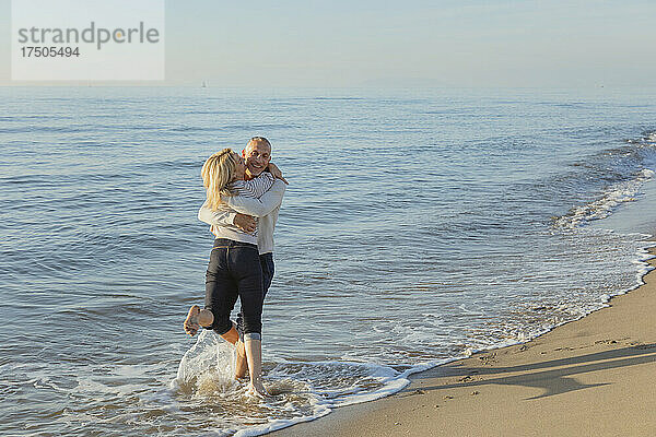 Mann spielt mit Frau im Wasser am Strand
