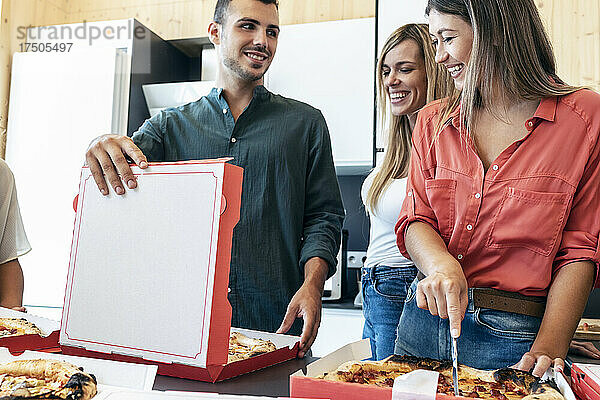 Lächelnde Geschäftsfrau  die von Kollegen im Büro Pizza schneidet