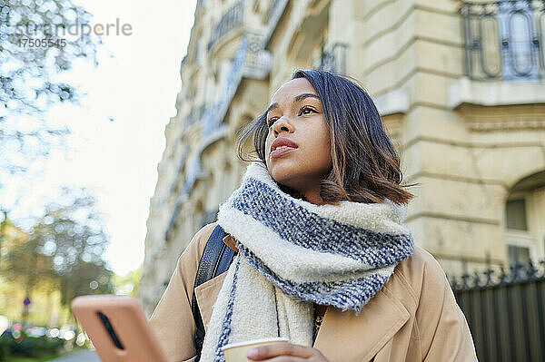 Nachdenkliche Frau mit Schal und Mobiltelefon in der Stadt