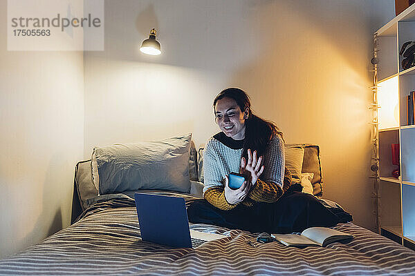 Lächelnde Frau begrüßt per Videoanruf über Laptop zu Hause
