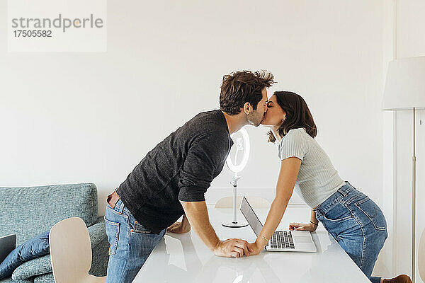 Junges Paar mit Laptop auf dem Tisch  das sich zu Hause küsst