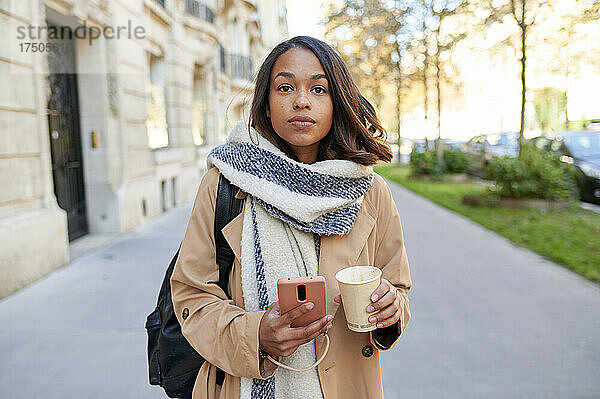 Frau hält Handy und Kaffeetasse auf Fußweg