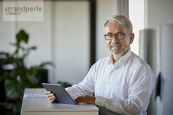 Lächelnder Geschäftsmann mit Tablet-Computer am Schalter im Büro
