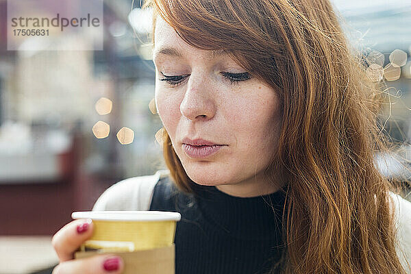 Frau bläst Kaffee in Einwegbecher im Café