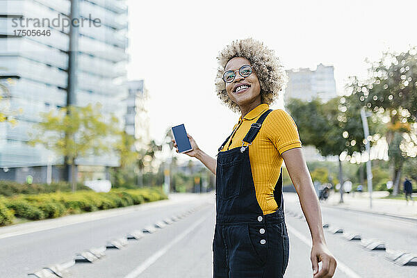 Lächelnde Frau mit Mobiltelefon auf der Stadtstraße
