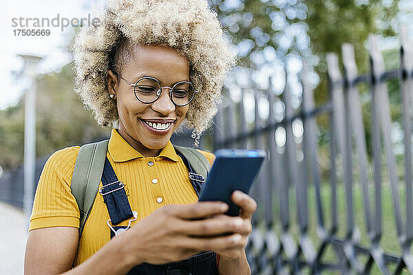 Lächelnde Frau mit Brille  die ihr Mobiltelefon benutzt