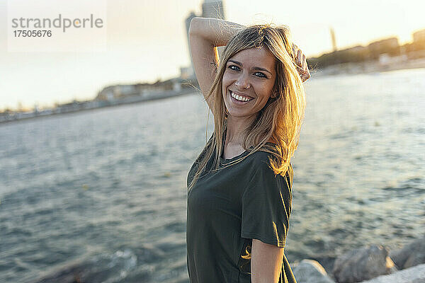 Lächelnde Frau mit der Hand im Haar am Strand von Bogatell  Barcelona  ??Katalonien  Spanien