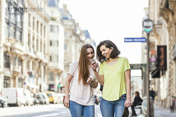 Lächelnde junge Frau zeigt ihrem Freund unterwegs ihr Mobiltelefon