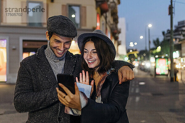 Glückliches junges Paar winkt per Videoanruf per Smartphone in der Stadt