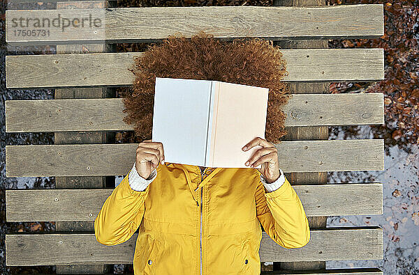 Frau bedeckt Gesicht mit Buch und liegt auf Brücke im Herbstwald