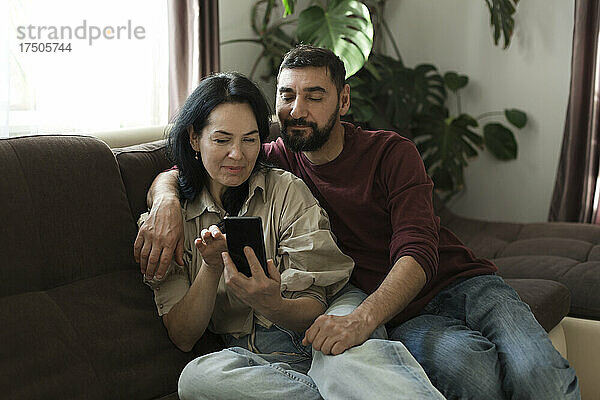 Paar benutzt Mobiltelefon zu Hause auf dem Sofa