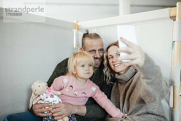 Lächelnde Frau  die zu Hause ein Selfie mit der Familie per Mobiltelefon macht