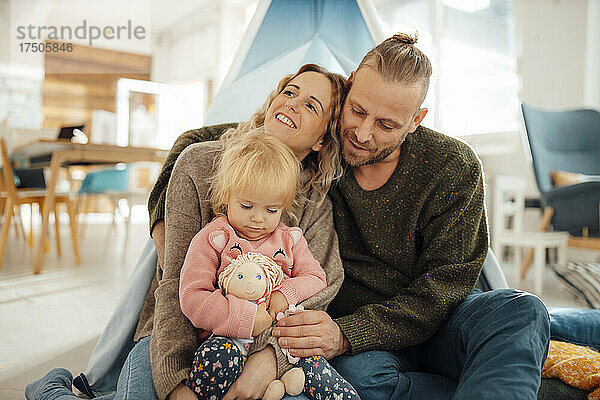 Mann umarmt Frau  die mit Mädchen zu Hause vor dem Zelt sitzt