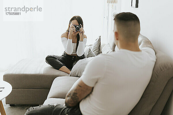 Frau fotografiert Mann mit Kamera im Wohnzimmer