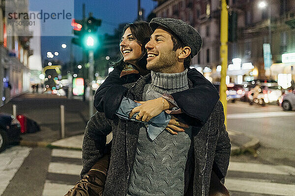 Glücklicher Mann trägt Freundin huckepack auf der Stadtstraße