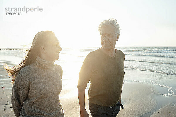 Lächelnde Frau mit Vater  die an einem sonnigen Tag am Strand spaziert