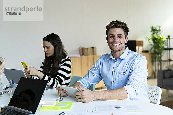 Arbeiter mit Tablet-PC sitzt mit Kollegen am Schreibtisch im Büro