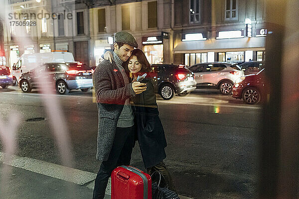 Junges Paar mit Rollgepäck nutzt Smartphone auf der Stadtstraße