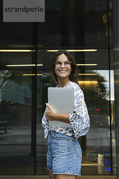 Lächelnde junge Geschäftsfrau mit Laptop  der wegschaut