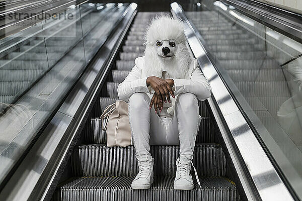 Frau mit Hundemaske sitzt auf Rolltreppe