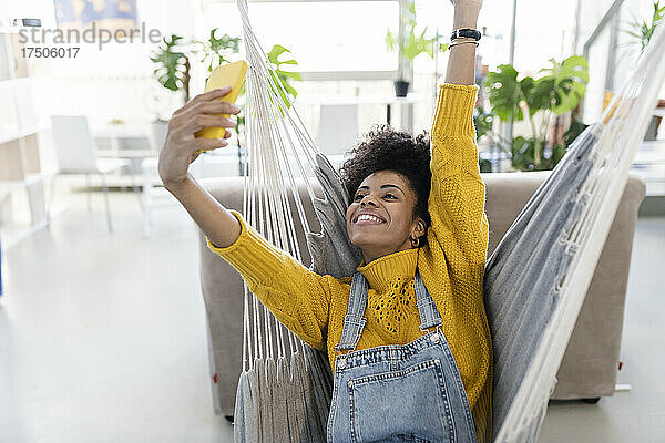 Lächelnde junge Frau  die zu Hause auf der Schaukel mit dem Smartphone filmt