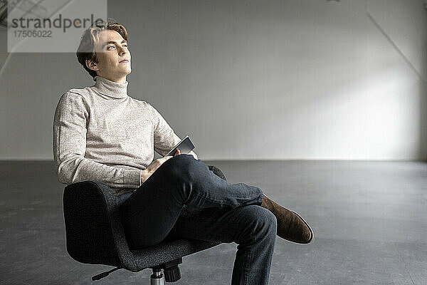 Hübscher Geschäftsmann  der auf einem Stuhl in einer leeren Industriehalle nachdenkt
