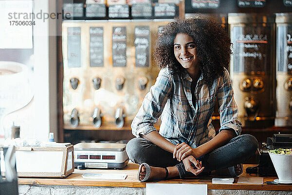 Geschäftsfrau sitzt mit gekreuzten Beinen auf der Theke einer Kaffeerösterei