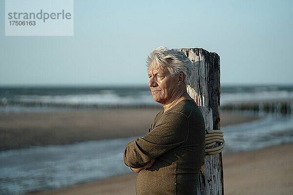 Älterer Mann stützte sich am Strand auf einen Holzpfosten