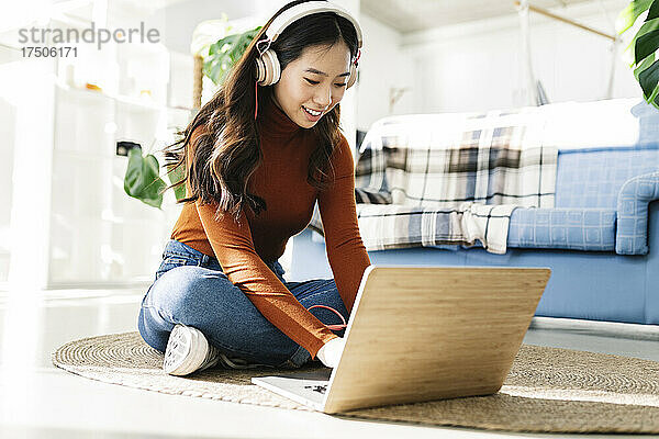 Geschäftsfrau mit Kopfhörern benutzt Laptop auf Teppich