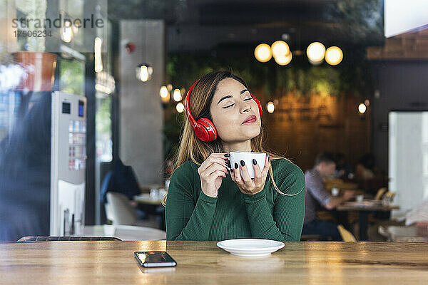 Frau mit Kaffeetasse hört Musik über Kopfhörer im Café